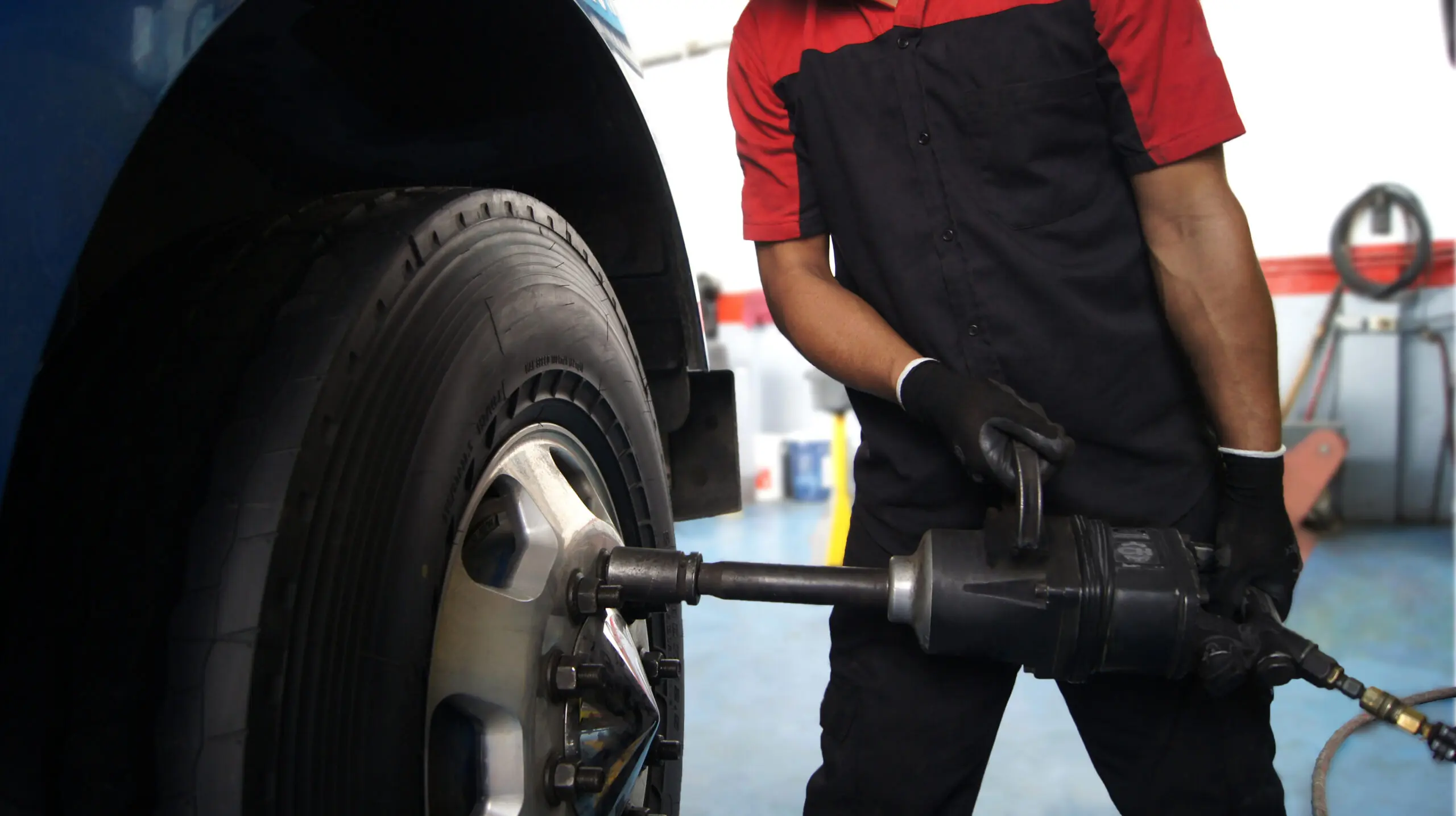 Mechanic changing tires on a truck using a pneumatic impact wrench in an auto repair shop. Close-up of the wheel and the maintenance process, representing professional automotive service.